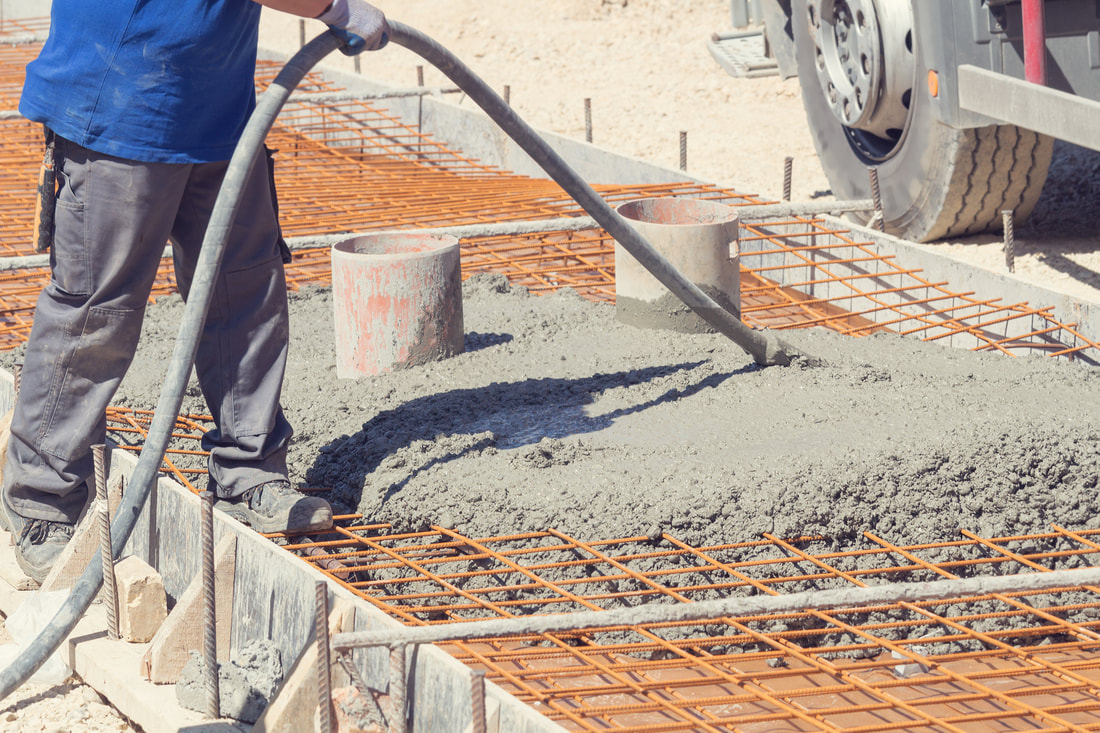 Man Standing on form of concrete using a vibration tool to vibrate the concrete down into voids in the rebar mats